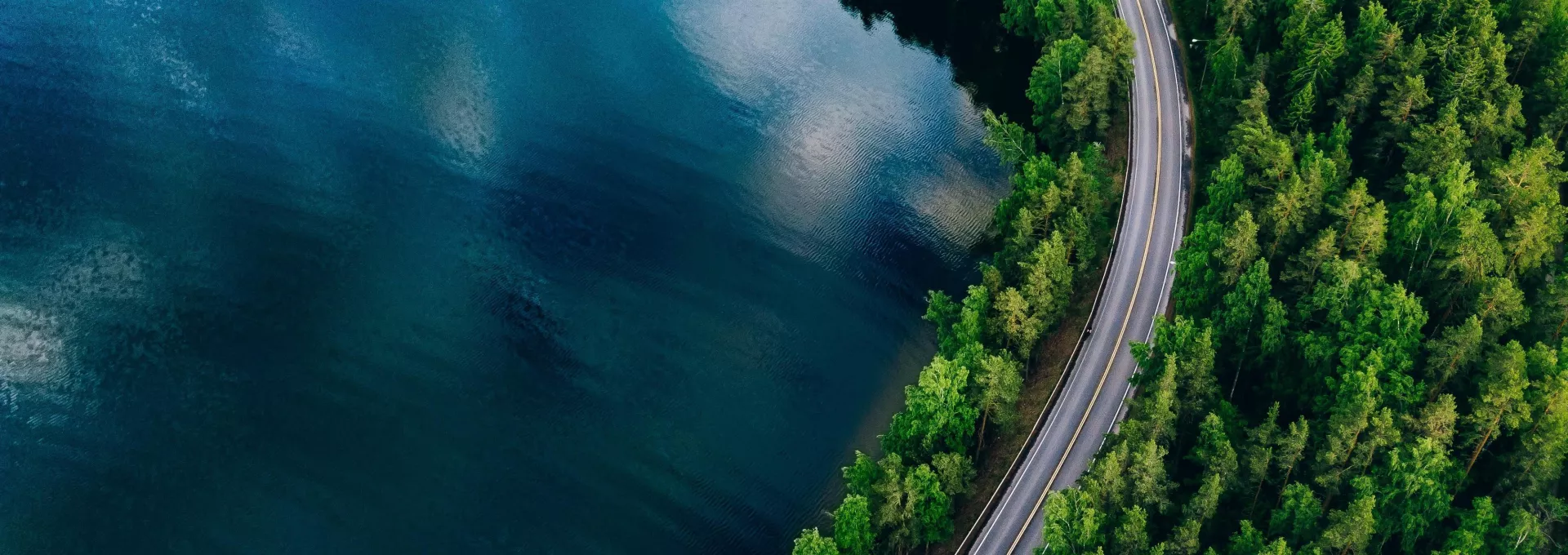 Aerial view of road between green forest and blue lake in Finland