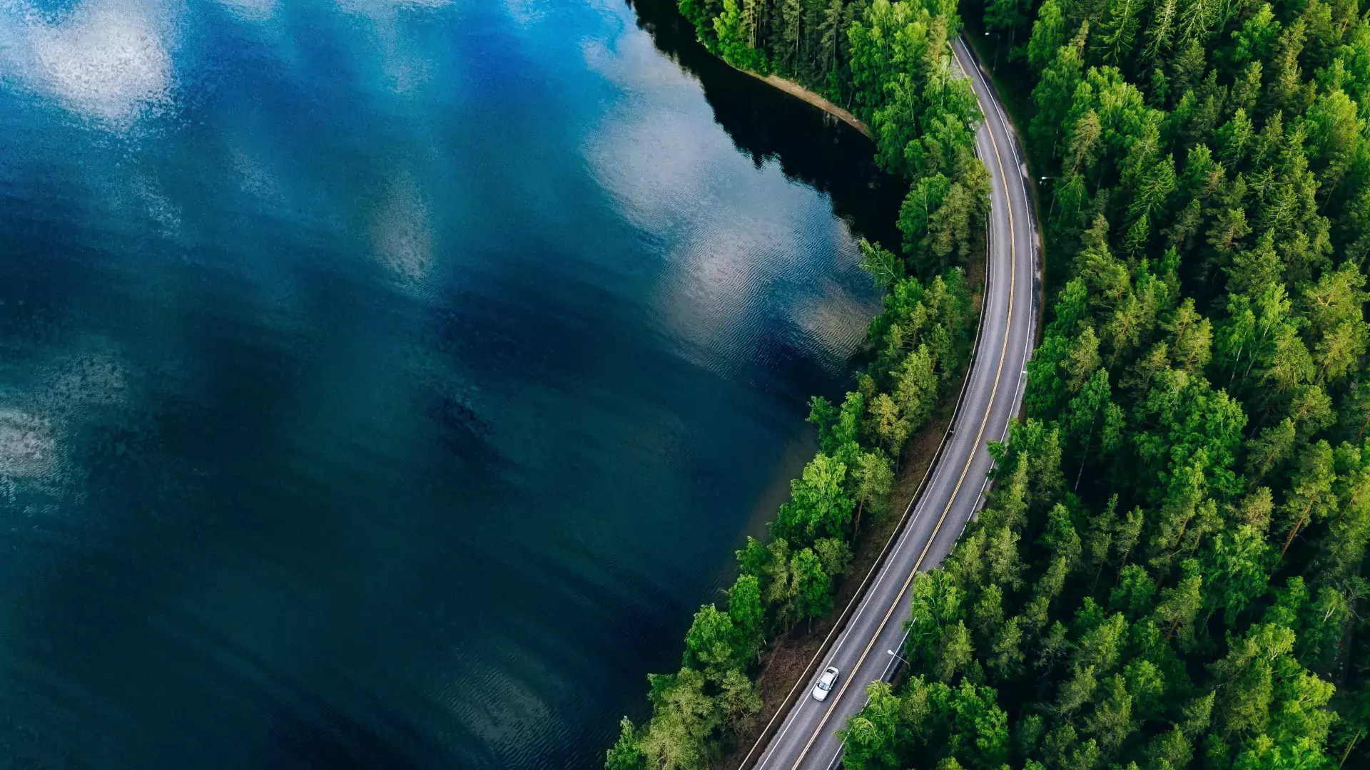 Aerial view of road between green forest and blue lake in Finland