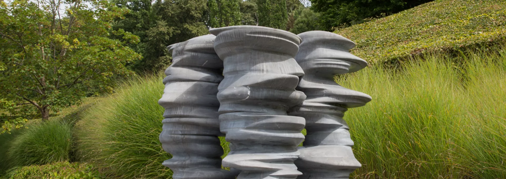 Grey stone sculpture in front of grass and trees