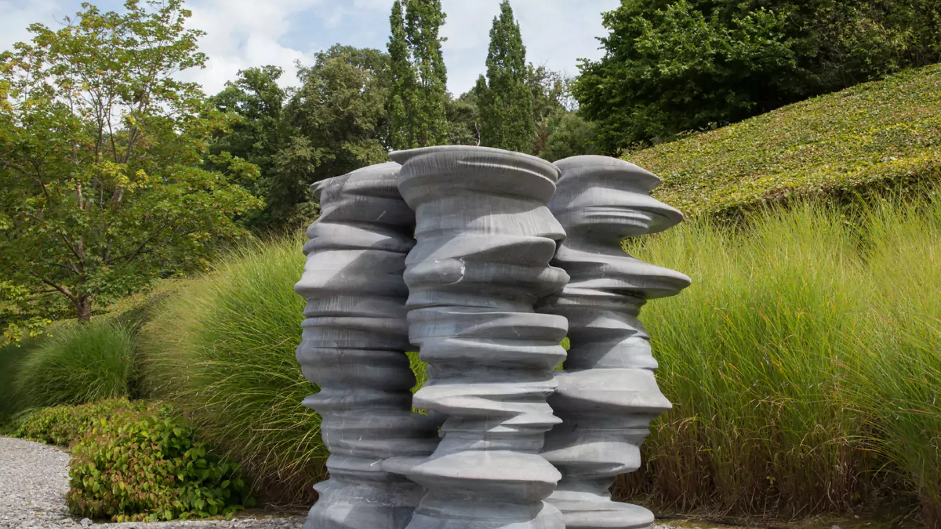 Grey stone sculpture in front of grass and trees