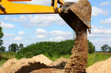 Yellow excavator shovel digging pit in ground