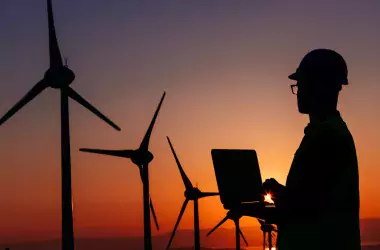 A person with computer in front of wind mills with sunset
