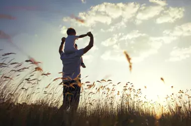 a man carrying his child on his shoulders in a field