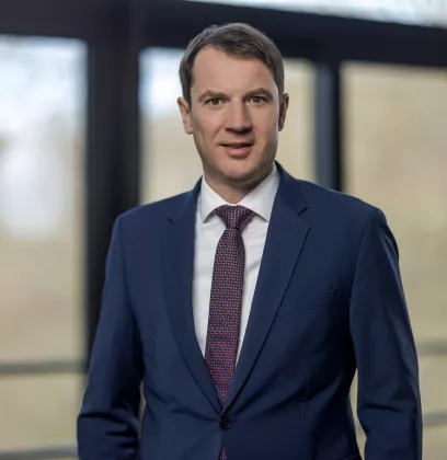 Business professional in a navy blue suit standing in a modern office environment with large windows and natural light.