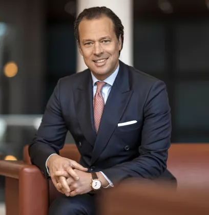 Business professional in a navy blue suit sitting on a brown sofa.