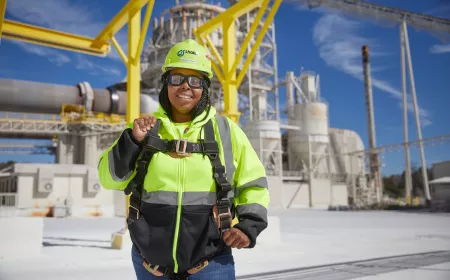 Smiling woman wearing a safety hardhat, glasses and reflective orange vest