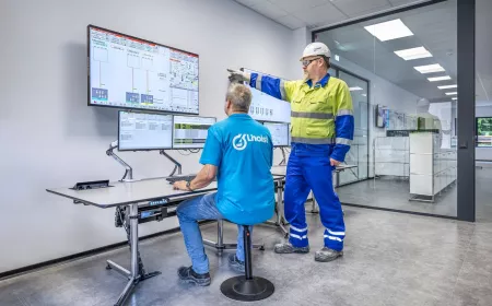 Two industrial workers monitoring and controlling production systems on multiple screens in a control room